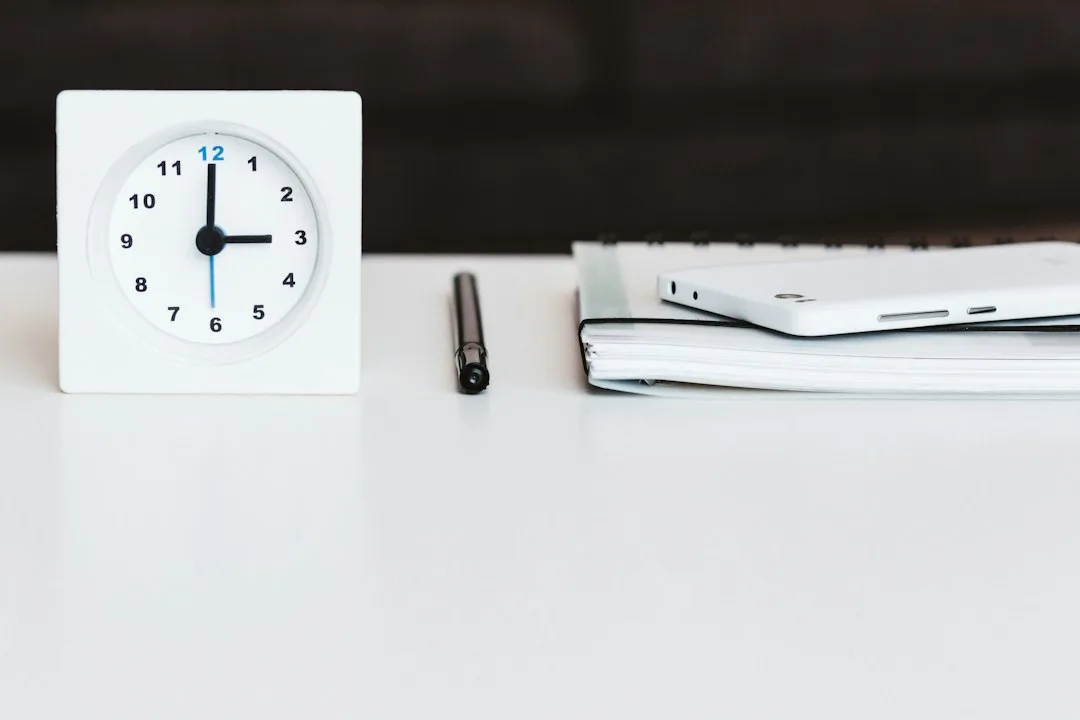 A desk clock beside a pen and notebook