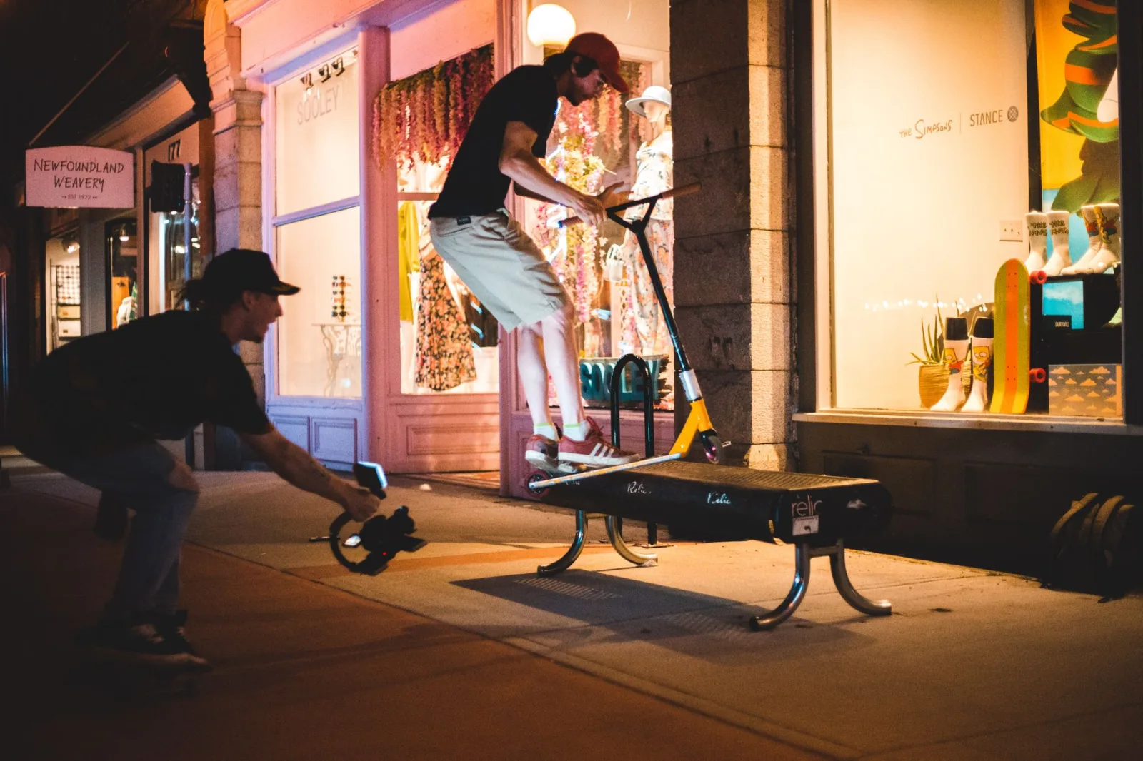 A young man filming his friend in the street at night, lit only by street lamps