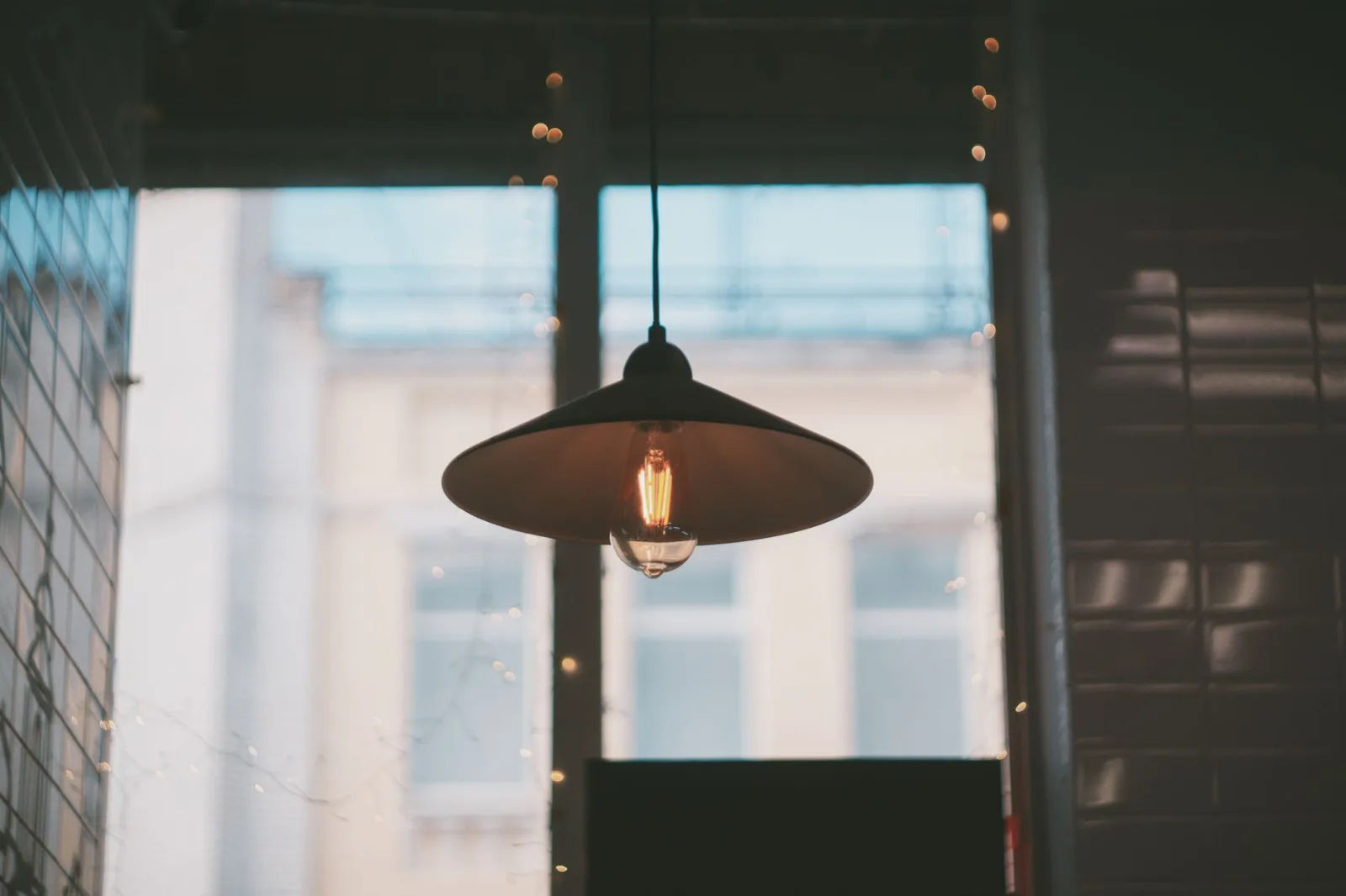 A room with a warm hanging lamp in front of a window, two lights of different colour mixing