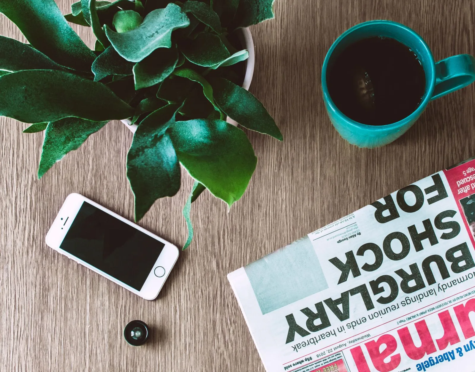 A newspaper, a phone and a coffee cup on a wooden table in the morning