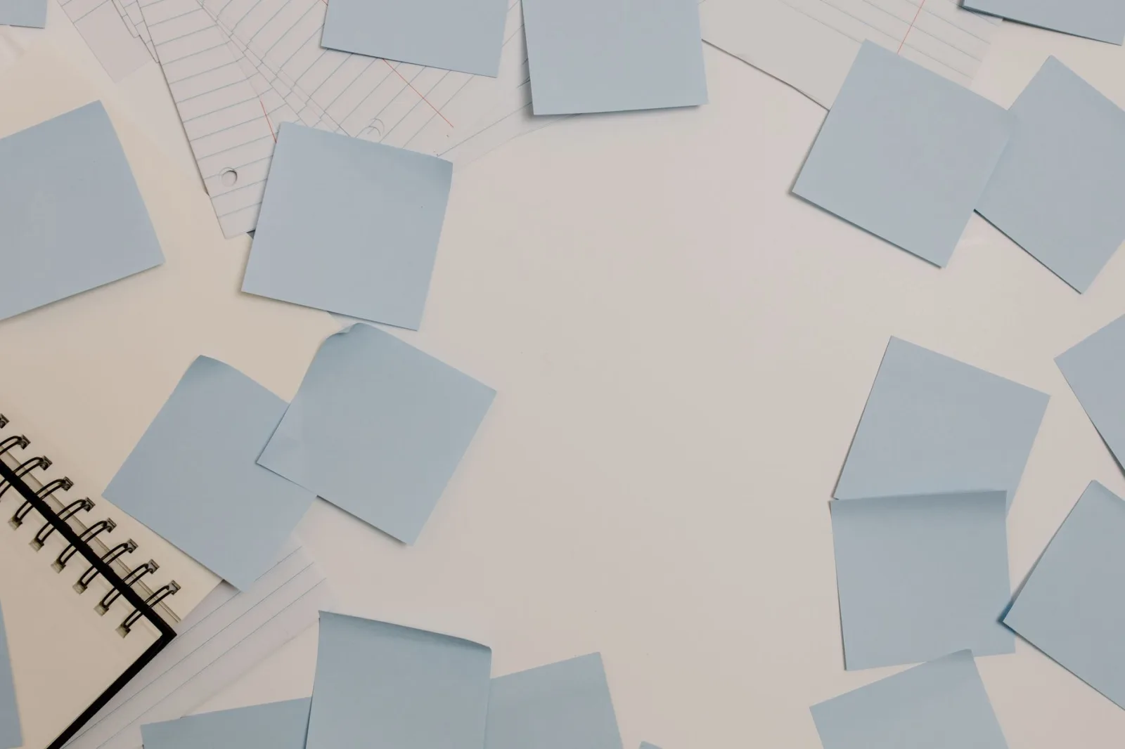 Sticky notes scattered across a desk beside a notepad and lined paper