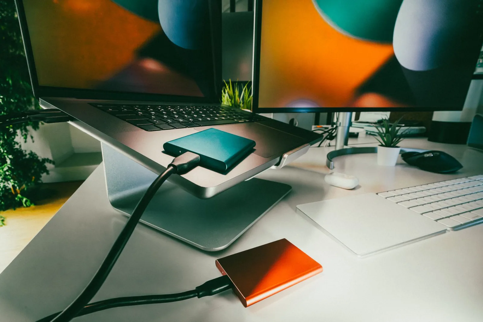A desk with a laptop and several external storage drives beside it