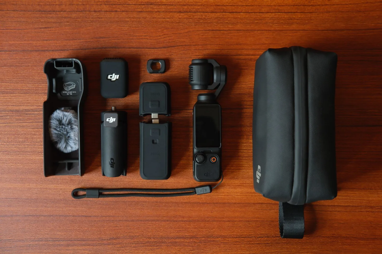 Compact filming gear laid out on a wooden table: camera, batteries, cards and cables