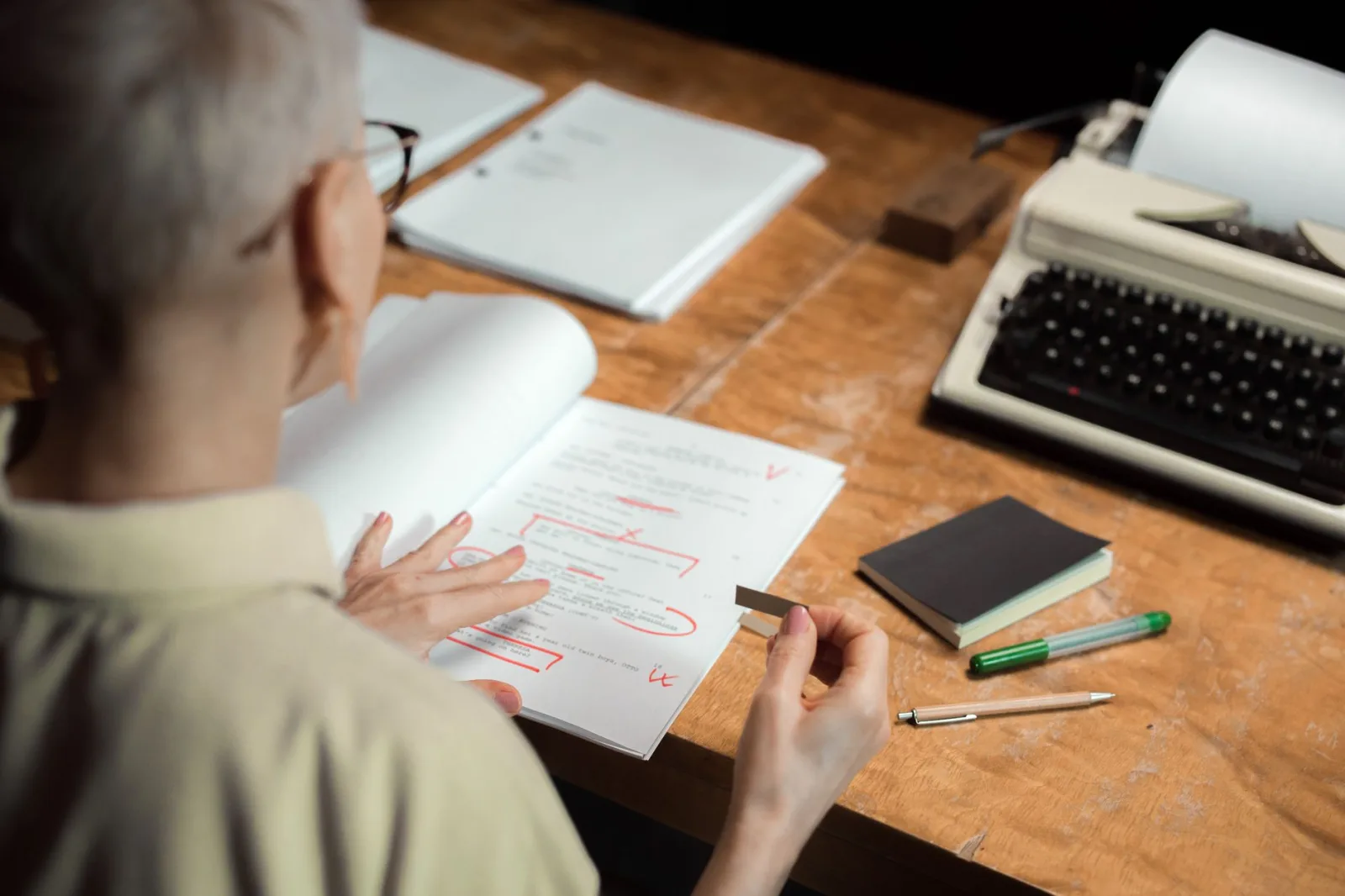 A person reviewing printed script pages marked up in red pen