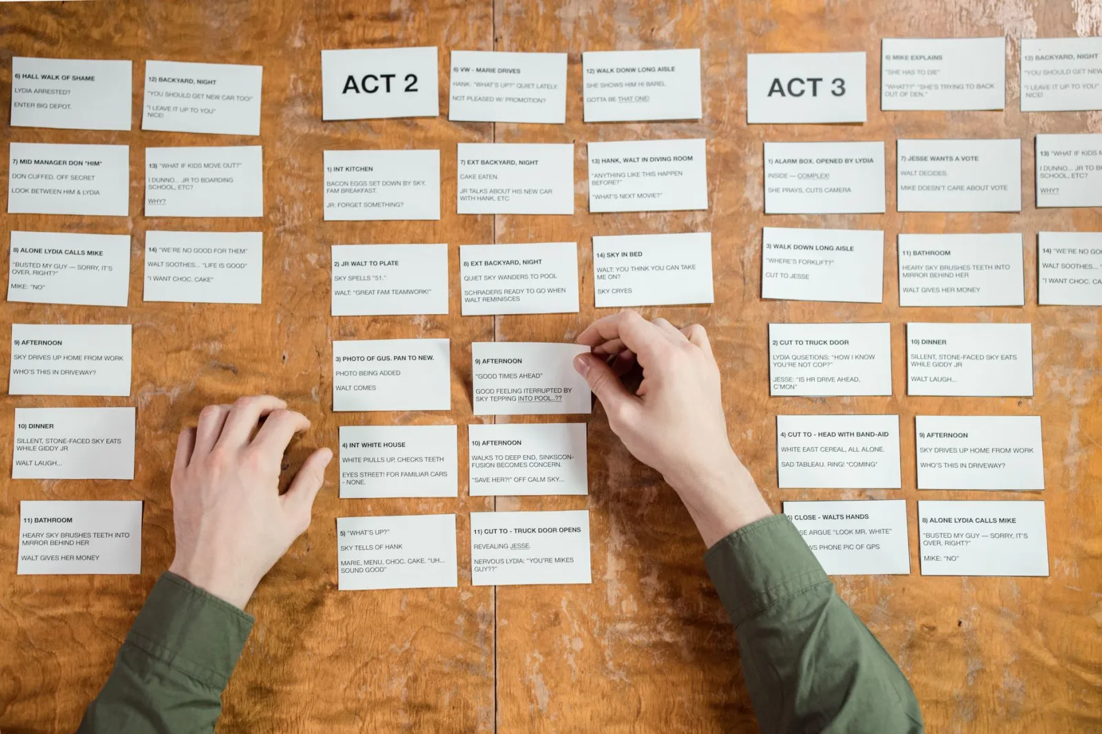 Hands arranging written cards in rows on a wooden table