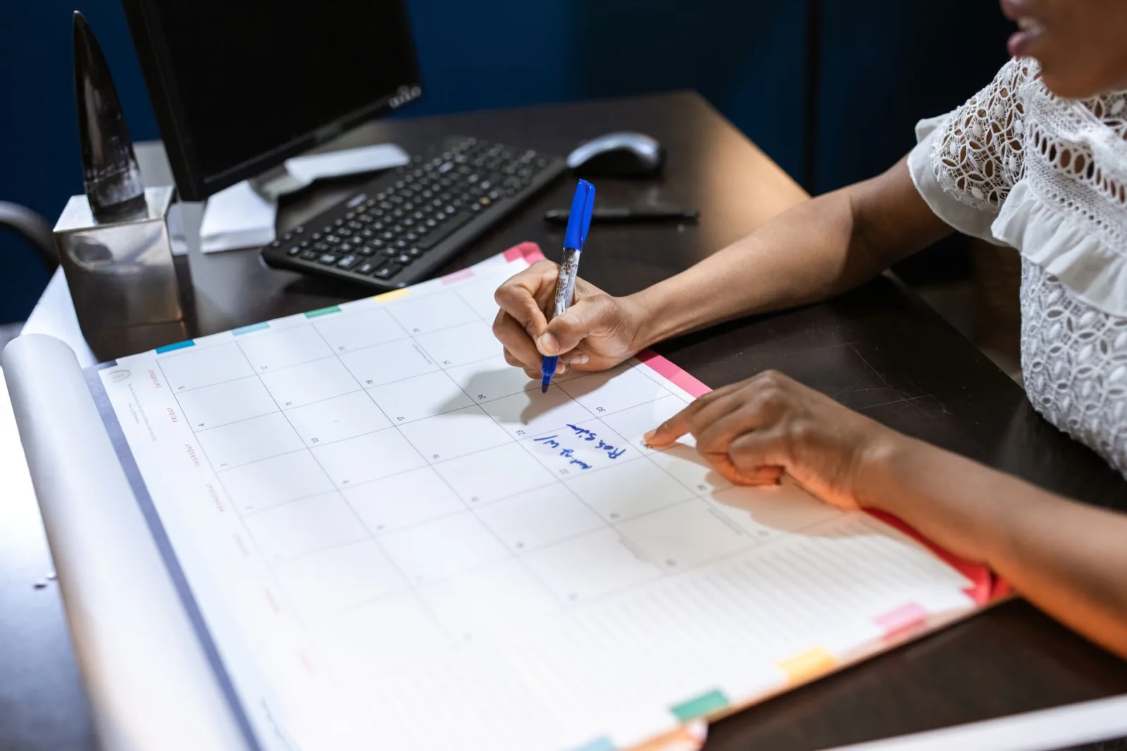 A person writing appointments into a monthly desk calendar